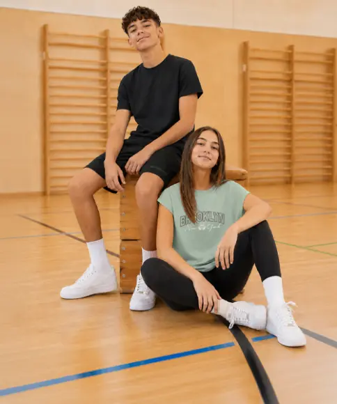 Dos adolescentes llevan ropa deportiva cómoda y están sentados sobre y junto a un potro de gimnasia. Sus outfits son ideales para las clases de educación física.